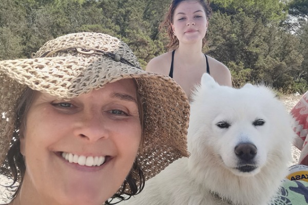 Frau mit Hut, Hund und Teenager sitzen am Strand